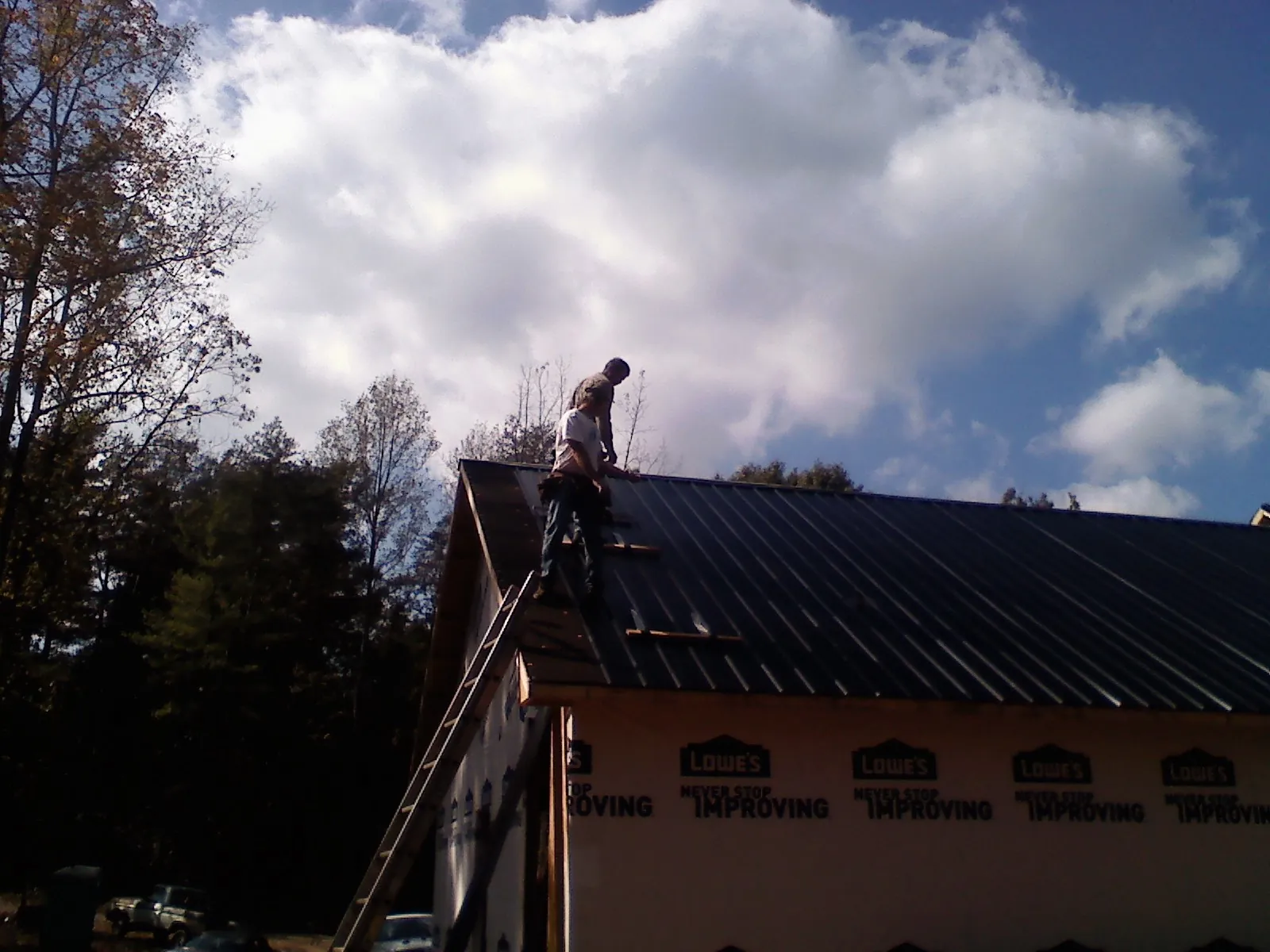 Roofer fastening dark metal panels high against a cloudy sky, from a Roof Inspection job in Fork Union