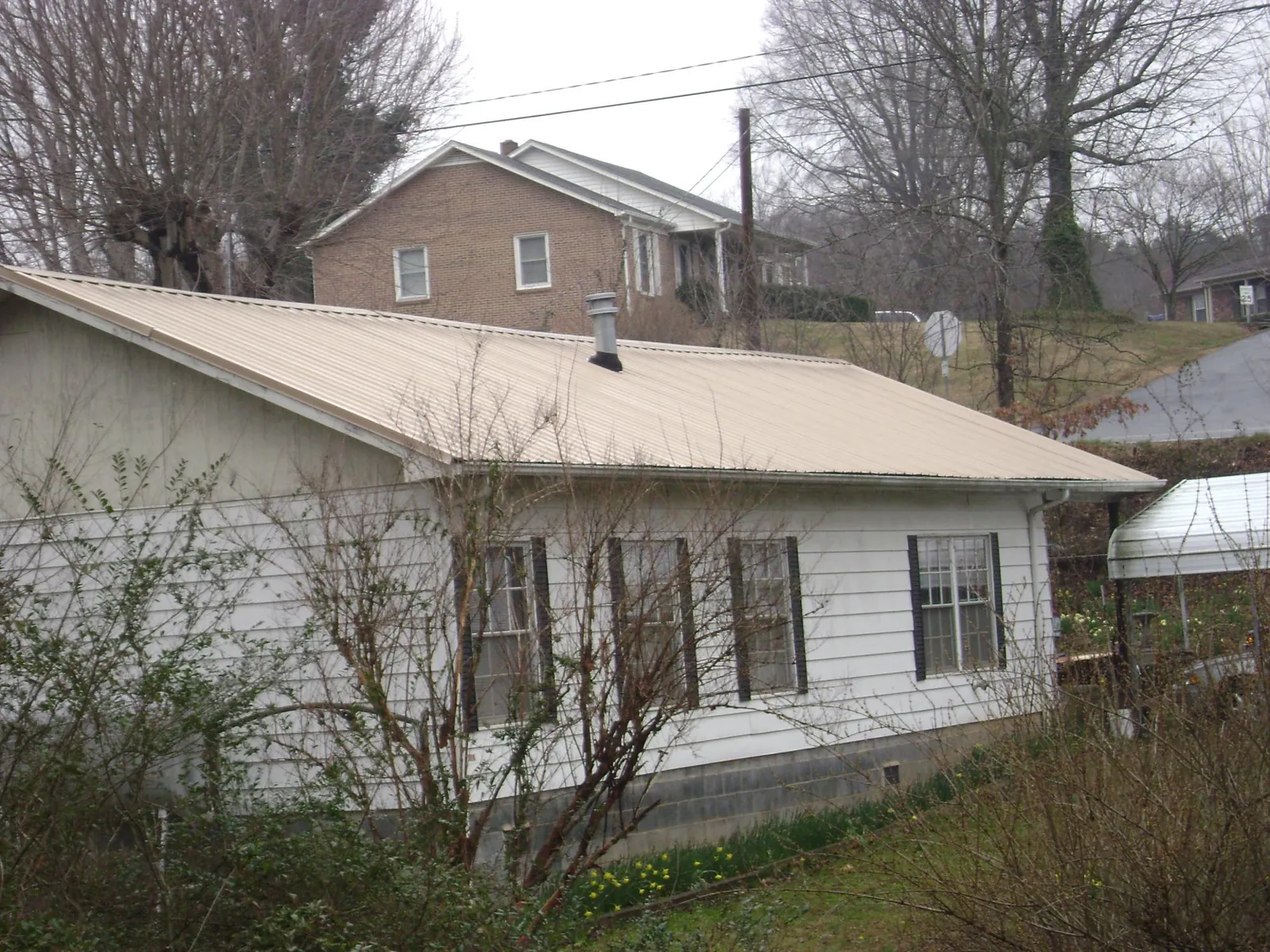 Tan metal roof on a white sided house set into a hillside — Commercial Roofing by Roofing Brothers in Fork Union